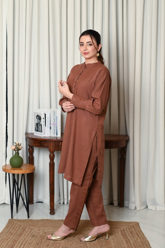 Woman in a brown outfit standing in a room with white curtains and a small table.
